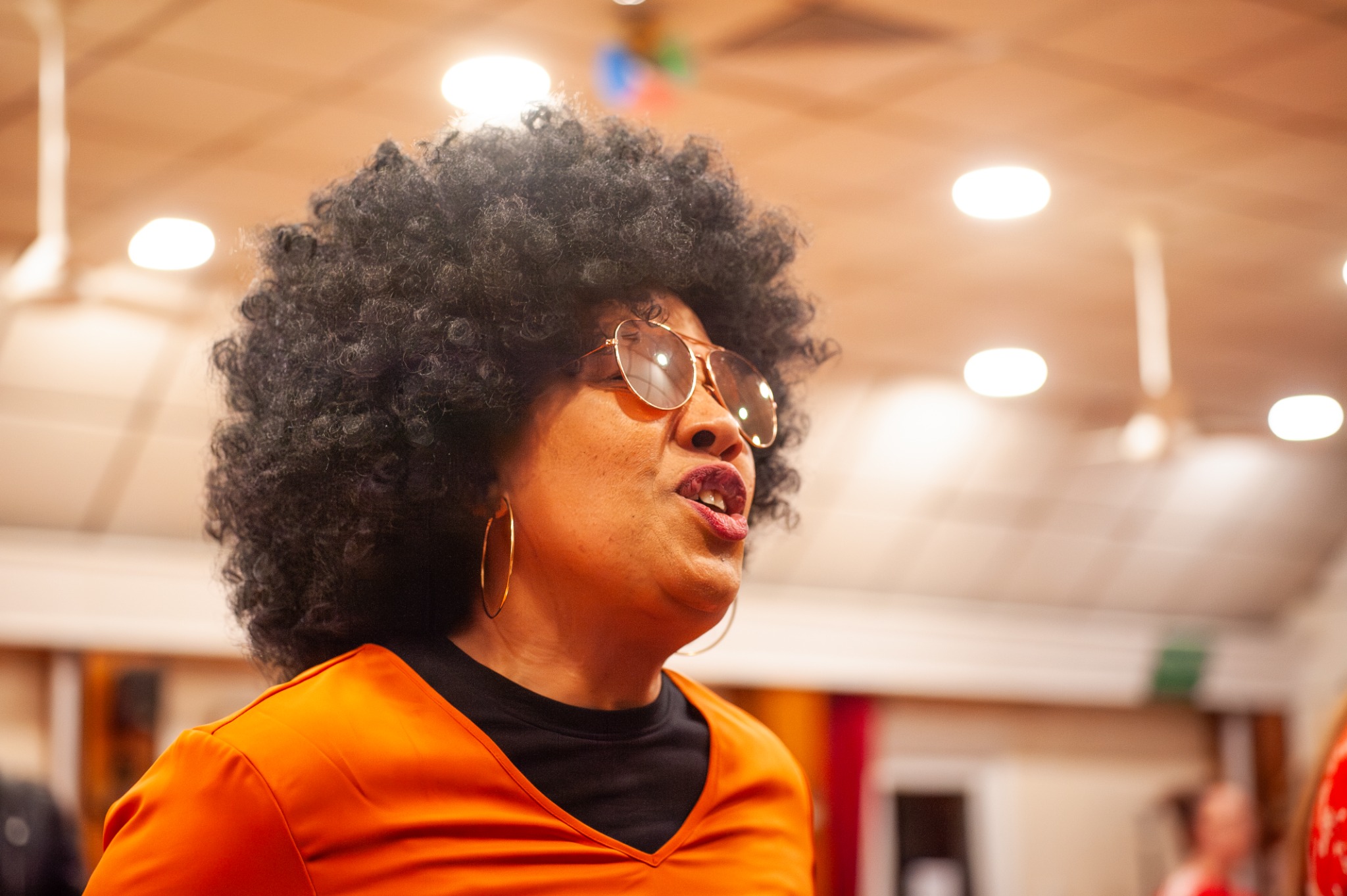 A performer singing in rehearsal, wearing orange and sunglasses