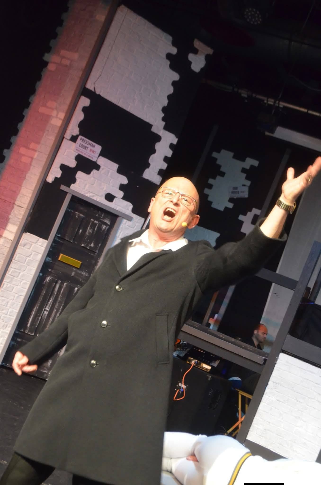 A performer in a dark suit raising one arm on stage