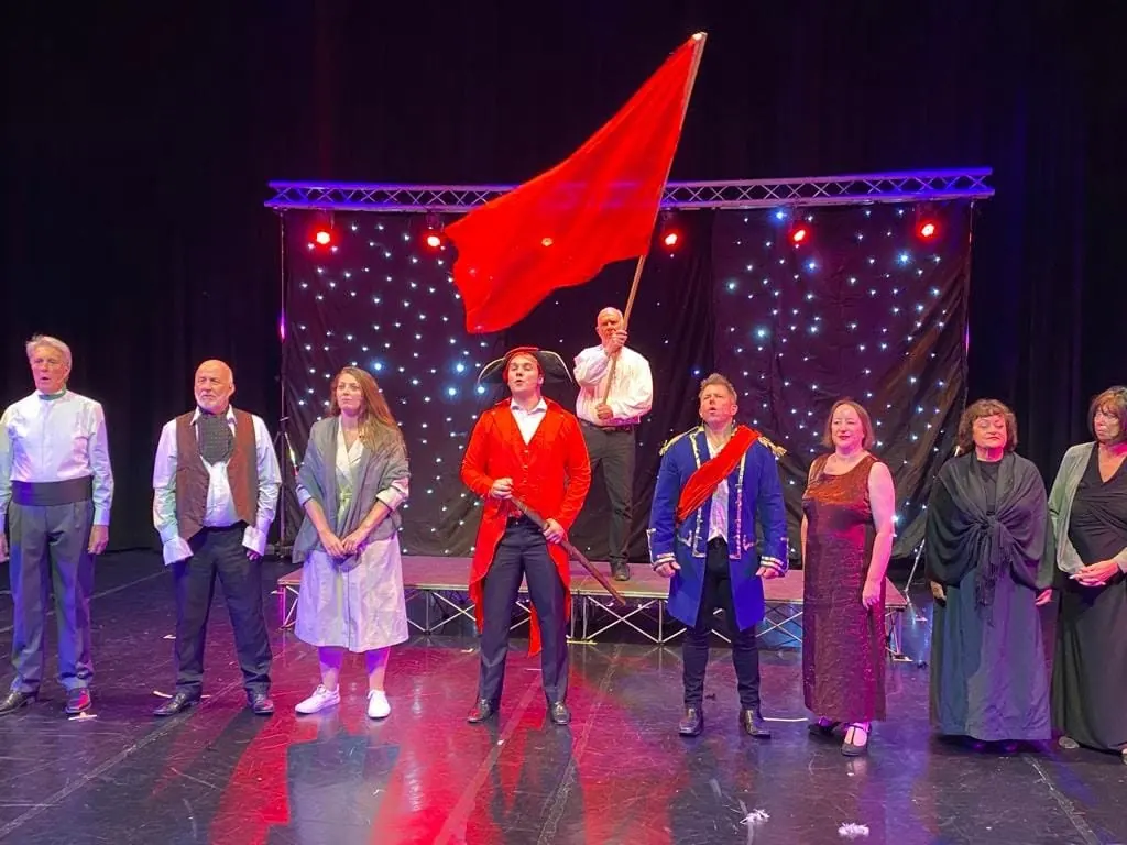 The company on stage beneath a large red flag