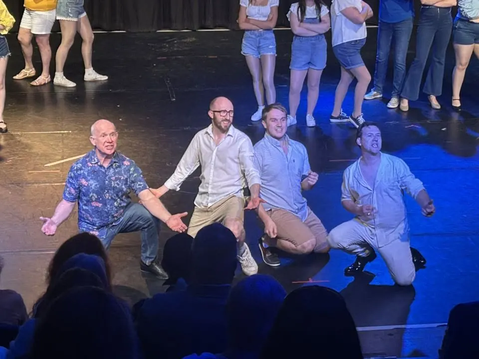 Three performers kneeling at the front of a rehearsal group
