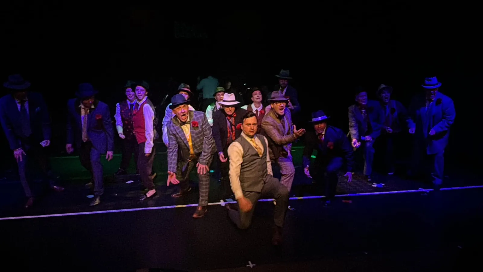 A performer in a waistcoat leading an ensemble under blue stage lights