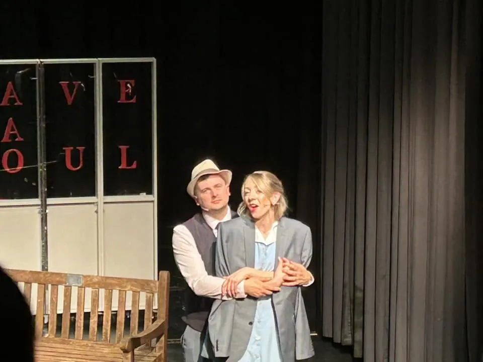 Two performers embracing beside a cafe set
